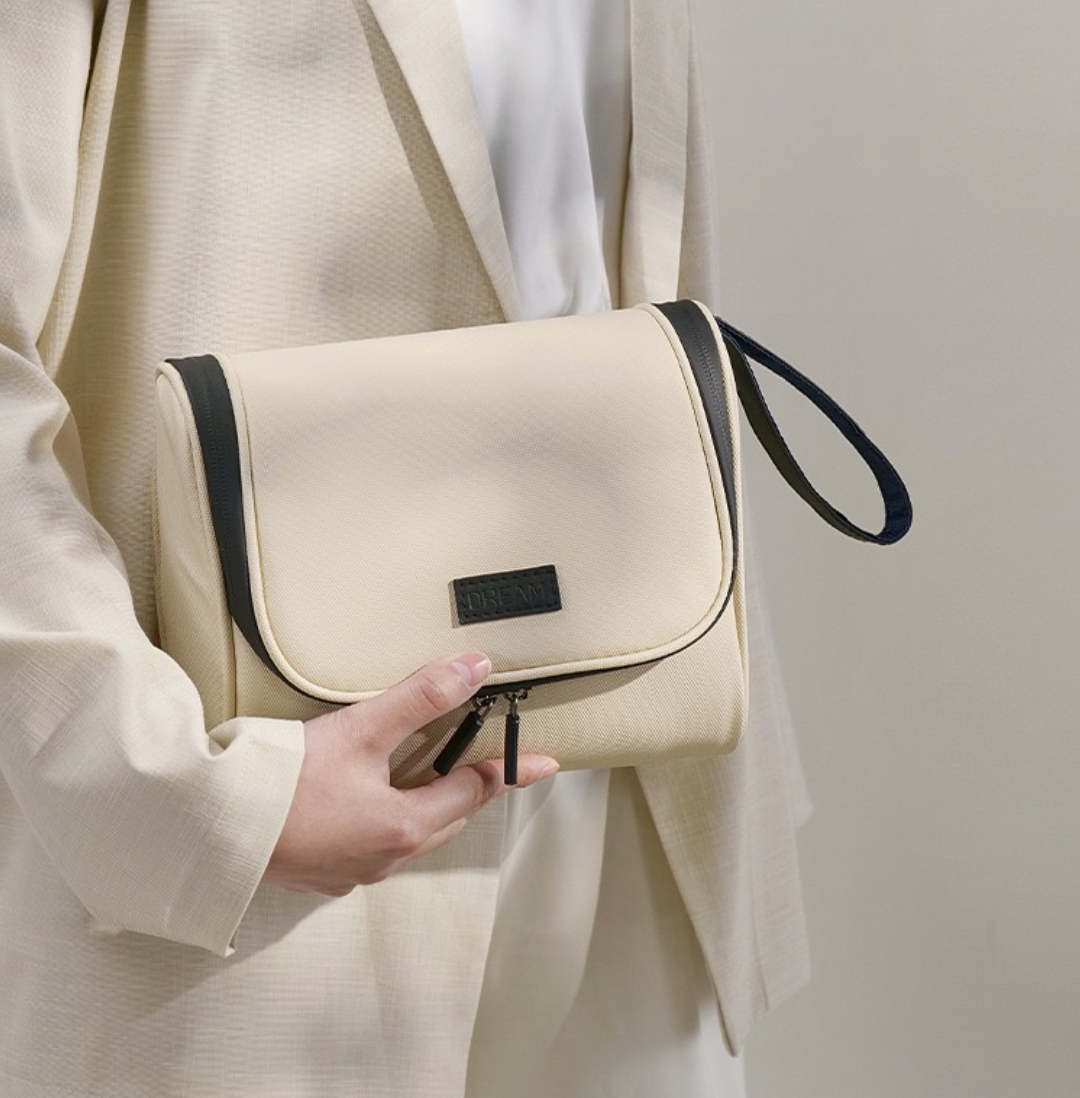 Beige handbag with black accents held by a person wearing a light-colored outfit on a neutral background